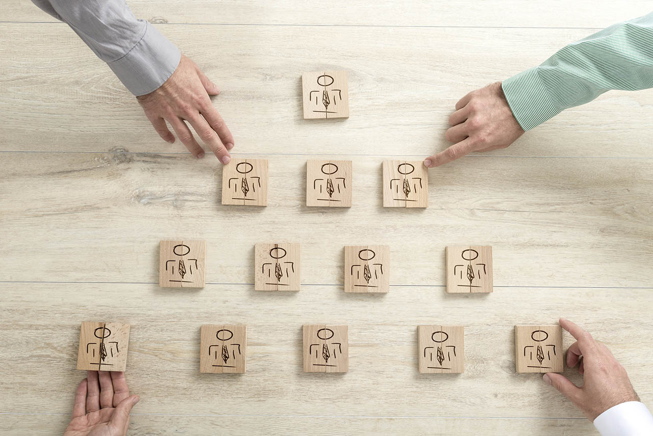 Pyramid of figures on wooden blocks with the hands of businessmen reaching out to touch four of them in a teamwork and human resources concept.